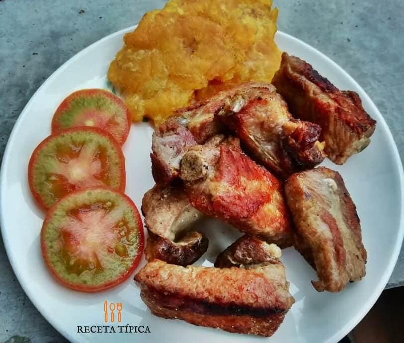 plato con costillas de cerdo al horno, tomates y patacones