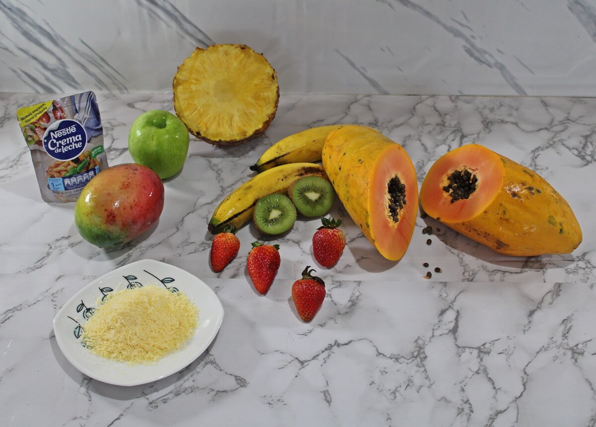 Ingredientes para preparar ensalada de frutas, fresas, papaya, kiwi, mango, queso parmesano, crema de leche, manzana, banano y piña